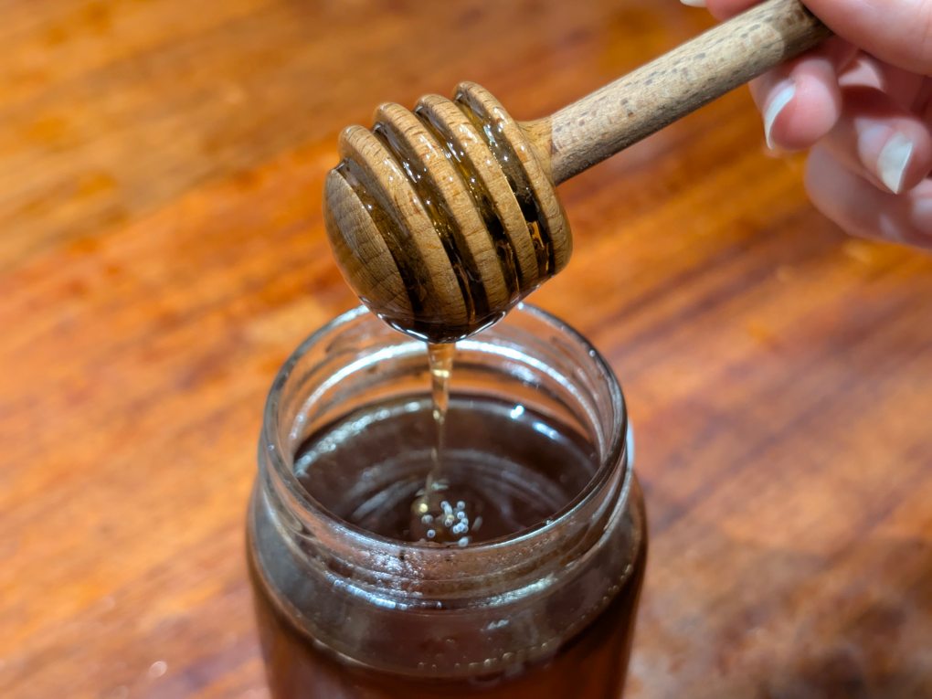 A wooden honey dipper with honey dripping into a jar