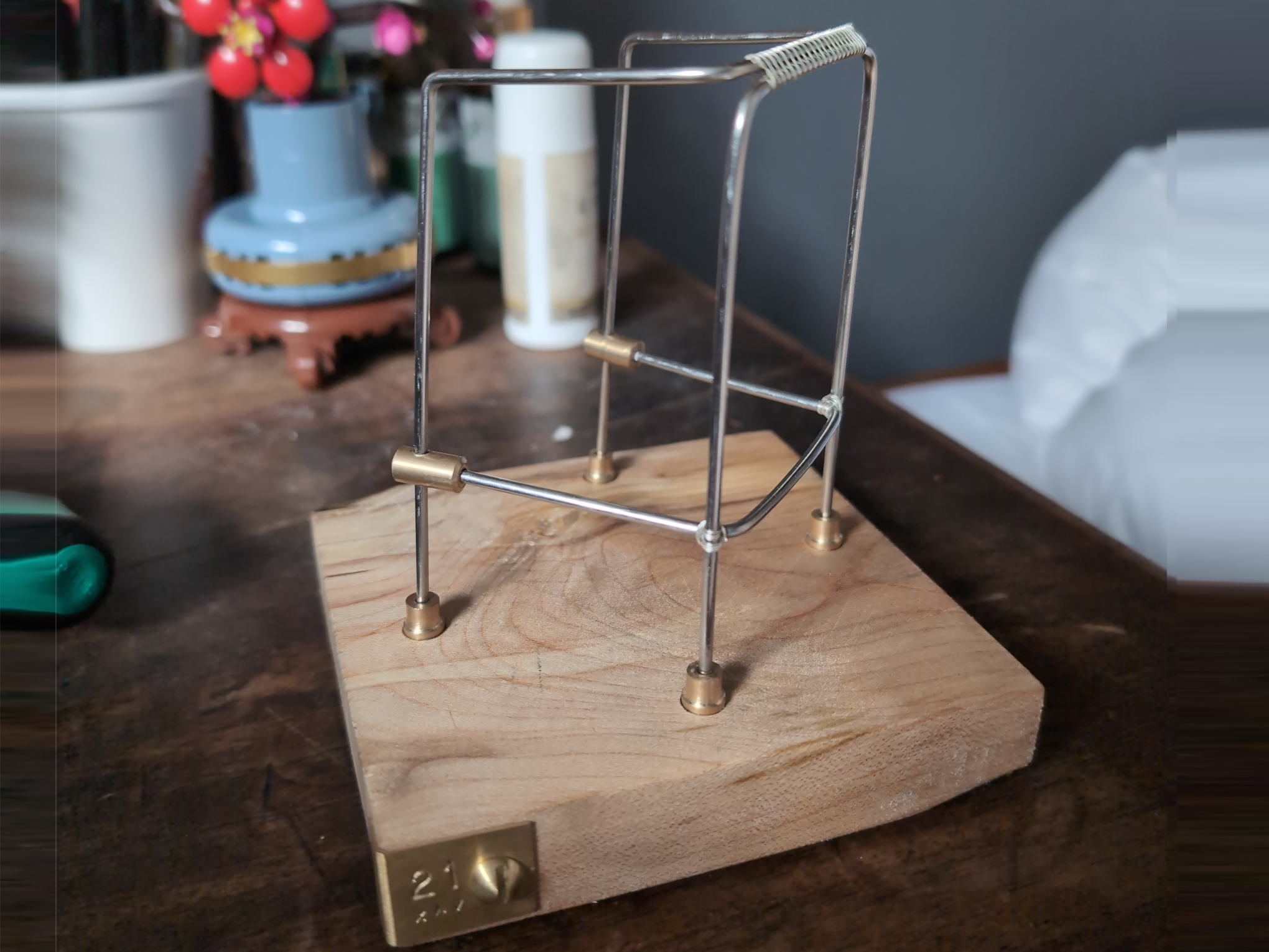 A silver wire zimmer frame with brass joints and silver wire wrapping on a wooden base